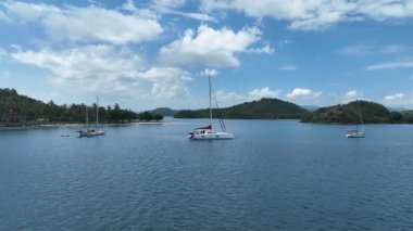 Kumlu bir sahile yakın, kristal berrak sular ve yoğun tropikal ormanlarla çevrili bir yatın manzarası. Huzurlu sahne cennetin özünü yakalar..