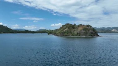 Kristal berraklığında bir göl, bu uzak ada cennetinde beyaz kumlu bir kıvrımla karşılaşır. Geleneksel tekneler kıyıya yakın süzülür, uzak tepeler ve ufukta mavi gökyüzü.