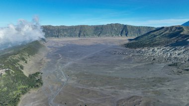 Kum denizinin çarpıcı kuş bakışı görüntüsü kaldera boyunca uzanır, kıvrımlı yollar ve yeşil sırtlar bu eşsiz volkanik manzarayı parlak mavi gökyüzü altında çerçeveler..