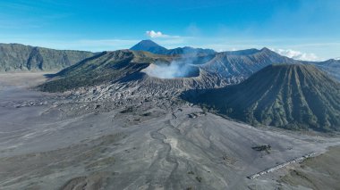 Kum denizinin çarpıcı kuş bakışı görüntüsü kaldera boyunca uzanır, kıvrımlı yollar ve yeşil sırtlar bu eşsiz volkanik manzarayı parlak mavi gökyüzü altında çerçeveler..