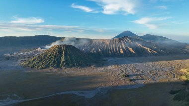 Görkemli krater Bromo manzaraya hükmediyor, dumanlı zirvesi ve sabah ışığında parlayan dik tepeleri, geniş kaldera ve uzak volkanik tepelerle çevrili..
