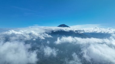 Gunung Agung bulut katmanının üzerinde dimdik duruyor, zirvesi açık mavi gökyüzüne yükseliyor ve yeryüzü ile cennet arasında çarpıcı bir zıtlık sunuyor..