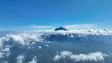 Agung Dağı bulutlardan oluşan bir denizin üzerinde görkemli bir şekilde yükselir, zirvesi mavi gökyüzünü delip geçer. Bu ikonik volkan Bali 'nin manzarasına hükmediyor, yukarıdan nefes kesici bir manzara sunuyor..