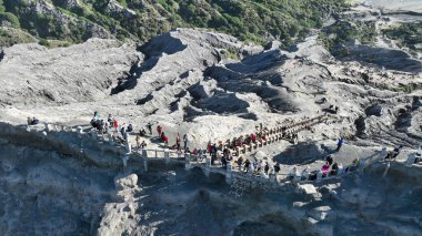 Volkanik kayalara oyulmuş dar bir merdivene tırmanan maceraperestlerin nefes kesici görüntüsü, dramatik gri yamaçlar ve uzaktaki yemyeşil tepelerle çevrili..