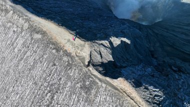 Antik bir volkanın jilet gibi kıyısında duran yalnız bir maceracı zaman ve doğa tarafından oyulmuş dramatik dokularla çevrili dumanlı uçuruma bakar..