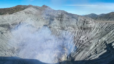 Engebeli bir volkanik kraterin kalbinden buhar yükseliyor, sarp duvarları antik yaralarla oyuluyor ve uzak dağ zirveleriyle çevrili..