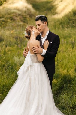 Genç ve güzel bir çift yeşil çimlerin üzerinde tepelerin arkasında sarılıyor. Yüksek kalite fotoğraf