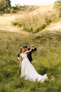 Genç ve güzel bir çift yeşil çimlerin üzerinde tepelerin arkasında sarılıyor. Yüksek kalite fotoğraf