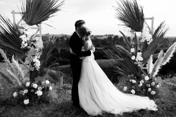 Black and white photo of a wedding couple hugging near the arch in nature. High quality photo
