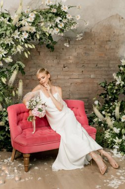 Gelinliği içinde gülümseyen güzel gelin parlak pembe kanepede oturuyor. Yüksek kalite fotoğraf