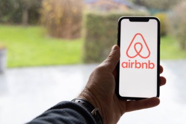 Paris, Fransa - 30 Kasım 2023 Airbnb uygulamalı akıllı telefonu tutan adam. Airbnb, insanların kısa vadeli konaklama veya kiralama olanağı sağlayan çevrimiçi bir pazar ve konaklama hizmetidir.