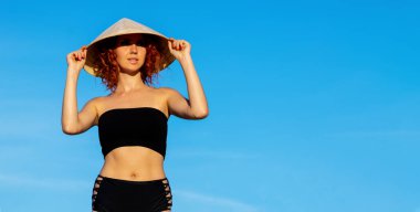 Mavi gökyüzü arka planında Asya tarzı konik şapkalı güzel bir kadın. Boşluğu, seyahat ve tatil belgesini kopyala.