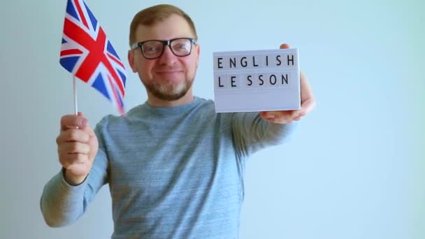 中世の男は眼鏡で英国の旗を持っています 先生は英語のレッスンという記号を指しています — ストック動画