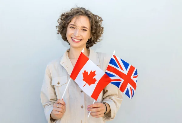 笑容可亲的女人举着英国和加拿大的国旗 在灰墙的背景上看着相机 — 图库照片