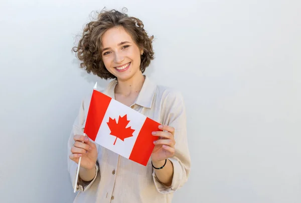 笑容可亲的女人举着英国加拿大国旗 在灰墙的背景上看着相机 加拿大教育 — 图库照片