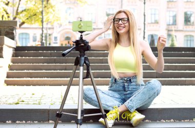 Genç kadın blogger basamaklarda otururken video akışı kaydediyor. Günlük sosyal medya videoları yap.