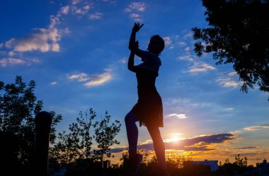 Mavi gökyüzüne ve günbatımına karşı dans eden genç bir kadının silueti. Özgürlük kavramı.