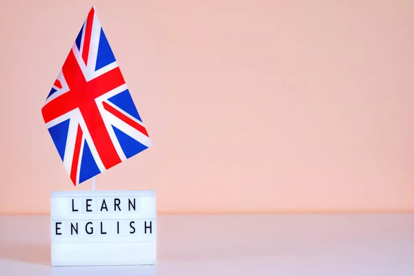 UK flag and text learn English on a pink wall background. Mockup for presentation about English courses.