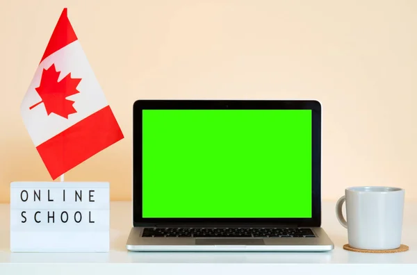 Open laptop with green screen chroma key on the table next to Canada flag and display that says Online School. Presentation mock-up for selling training via the Internet.