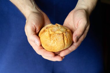 Erkek fırıncı taze pişmiş küçük bir somun ekmek tutuyor, elleri yakın plan..
