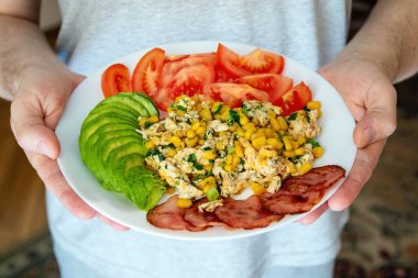 İçinde yeşil avokado, kırmızı domates, mısır ezmesi ve pastırma olan bir tabak dolusu erkek eli. Sabah kahvaltısını hazırla..
