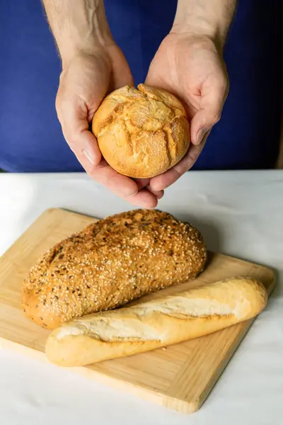 Man holding freshly baked assorted breads, hands close up. Vertical photo.