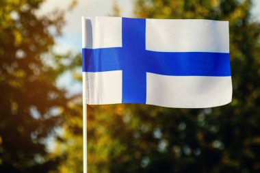 Yeşil bitkilerin arka planında Finlandiya bayrağı ve bulutlu mavi gökyüzü. 