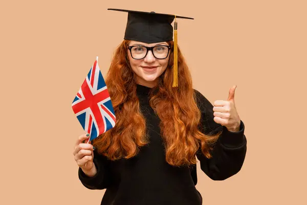 Female Student Wearing Flag Glasses Showing Thumbs Wearing Bachelor Cap Imagen de archivo