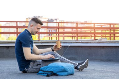 Genç adam laptopla çalışıyor, çatıya çıkıyor. Erkek Serbest İşçi.