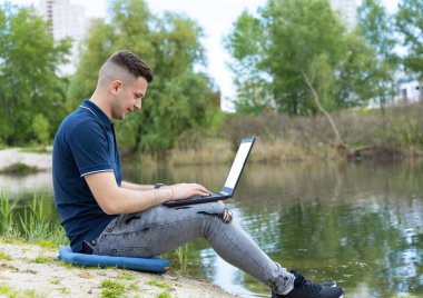 Genç adam dışarıdayken bir dizüstü bilgisayarda çalışıyor. Çevreyi araştıran bağımsız bir ekolojist. Dışarıda çalışmak ofisin en iyi alternatifi..