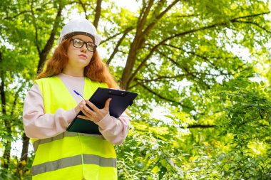Kadın çevreci. Elinde dosya olan mühendis kadın ormandaki ağaçları kontrol ediyor. Orman kontrolü.
