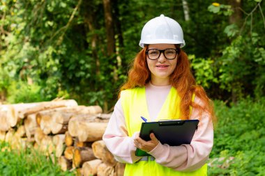 Orman mühendisi koruyucu giysi işçisi, kereste kesim ağacının önünde. Ağaçları kontrol eden ekolojist kadın. Çevre denetimi.