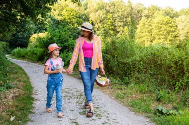 Anne ve kızı bir orman parkında birlikte yürüyorlar. Bir kadın ve bir kız aile pikniğine gidiyorlar..