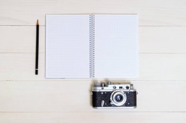 Fotoğraf makinesi, kalem ve spiral defter. Fikirleri yazmak için. Düz bir şekilde tahta masaya uzanıyordu..