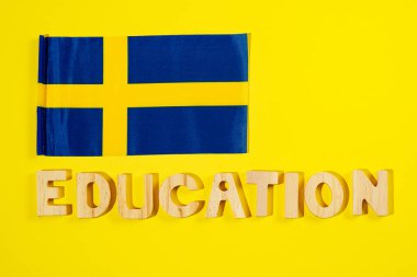 İsveç bayrağı ve ahşap harfli kelime eğitimi sarı arka planda.