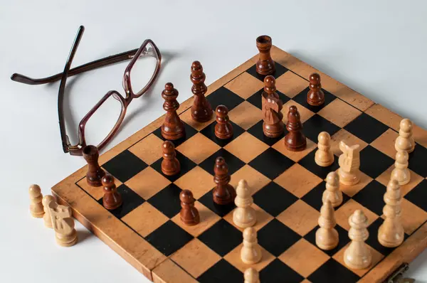 Fotoğraftaki satranç tahtası beyaz tabanlı ve arka planda satranç oyuncularının gözlüklerinin eklenmesi ile birlikte.