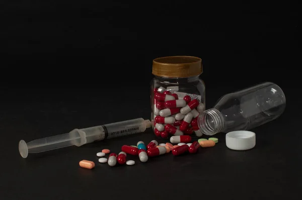 İlaç şişesinin içindeki, şişenin dışına ve yanına saçılmış bir şırınga. Kullanımı ve dozajına uygun değilse ilaç kullanmanın tehlikelerini gösteren koyu bir arka planı var.