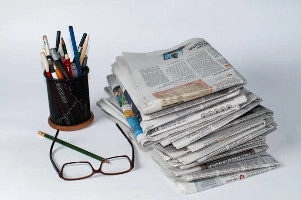 İş ve finans haberleri için okunması gereken bir yığın gazetenin yanı sıra masaya konmuş kırtasiye ve bardaklar, hafif bir arkaplan kullanarak fotoğraf çekiliyor.
