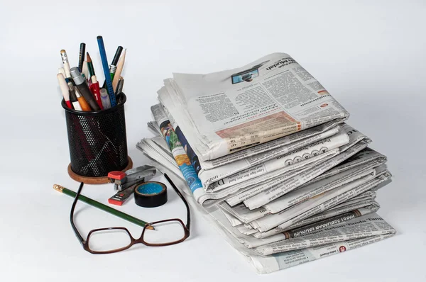 İş ve finans haberleri için okunması gereken bir yığın gazetenin yanı sıra masaya konmuş kırtasiye ve bardaklar, hafif bir arkaplan kullanarak fotoğraf çekiliyor.