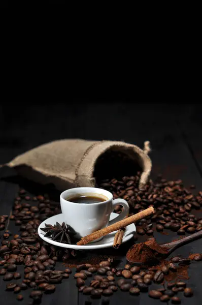 Kahve çekirdekleri, tarçın ve koyu arkaplanda çekilmiş bir fincan sade kahve.