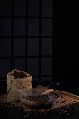 Kahve değirmeninin fotoğrafı, kahve çekirdeği, kahve kaşığı, kahve fincanı ve koyu bir pencere arkasında kahve çekirdeği.