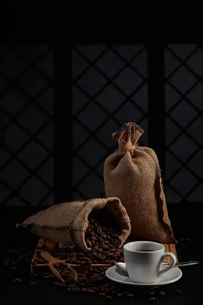 Kahve değirmeninin fotoğrafı, kahve çekirdeği, kahve kaşığı, kahve fincanı ve koyu bir pencere arkasında kahve çekirdeği.