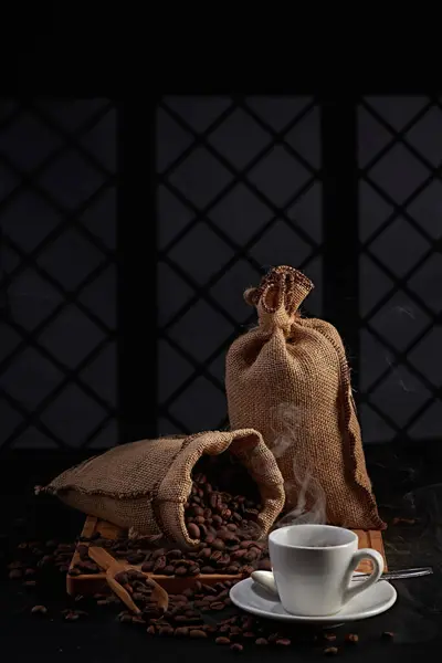 Kahve değirmeninin fotoğrafı, kahve çekirdeği, kahve kaşığı, kahve fincanı ve koyu bir pencere arkasında kahve çekirdeği.