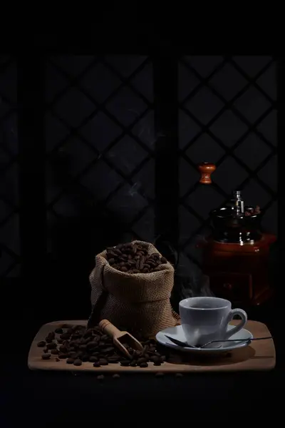 Kahve değirmeninin fotoğrafı, kahve çekirdeği, kahve kaşığı, kahve fincanı ve koyu bir pencere arkasında kahve çekirdeği.