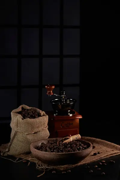 Kahve değirmeninin fotoğrafı, kahve çekirdeği, kahve kaşığı, kahve fincanı ve koyu bir pencere arkasında kahve çekirdeği.