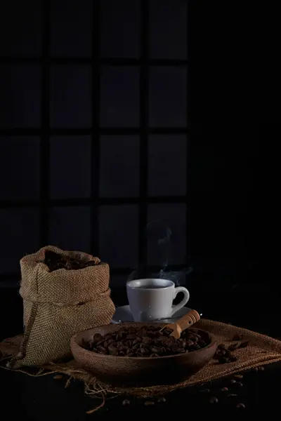 Kahve değirmeninin fotoğrafı, kahve çekirdeği, kahve kaşığı, kahve fincanı ve koyu bir pencere arkasında kahve çekirdeği.