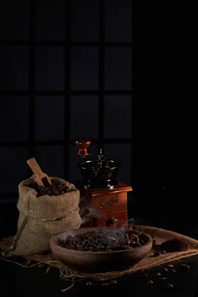 Kahve değirmeninin fotoğrafı, kahve çekirdeği, kahve kaşığı, kahve fincanı ve koyu bir pencere arkasında kahve çekirdeği.