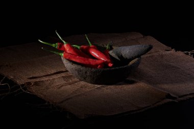 Büyük kırmızı ve yeşil biberler, hafif dumanla karakterize edilmiş baharatlı bir biber sosu yapmak için, taş havan ve tokmakla dövülmeye hazırdır..