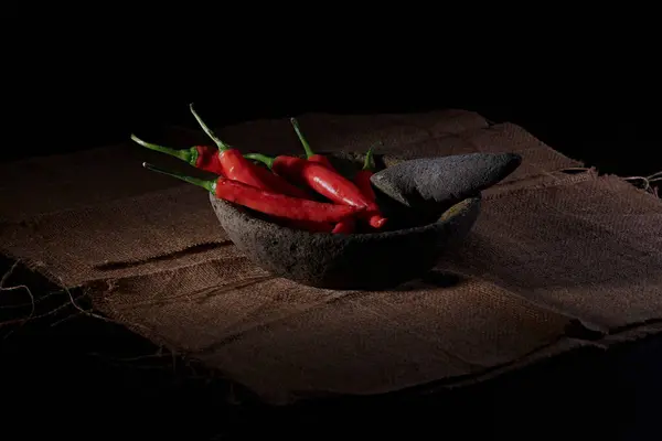 Büyük kırmızı ve yeşil biberler, hafif dumanla karakterize edilmiş baharatlı bir biber sosu yapmak için, taş havan ve tokmakla dövülmeye hazırdır..