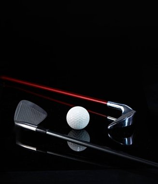 Golf sopası ve golf topu karanlık bir arkaplanda fotoğraflanmış ve fotoğrafta yansımalar var.